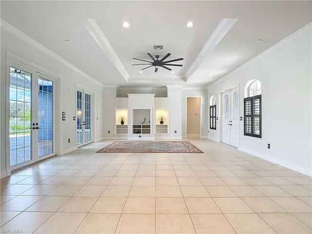 Unfurnished living room featuring french doors, a raised ceiling, ornamental molding, recessed lighting, and light tile patterned floors