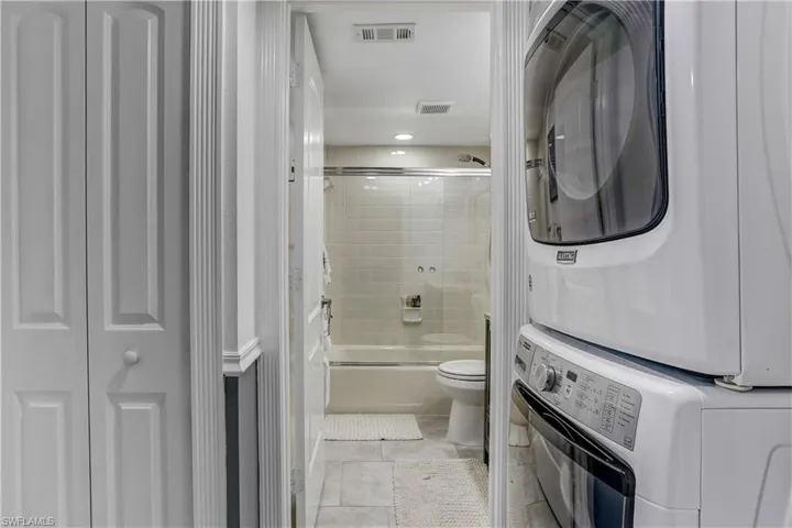 Full bathroom with a closet, stacked washing machine and dryer, enclosed tub / shower combo, recessed lighting, and light tile patterned flooring