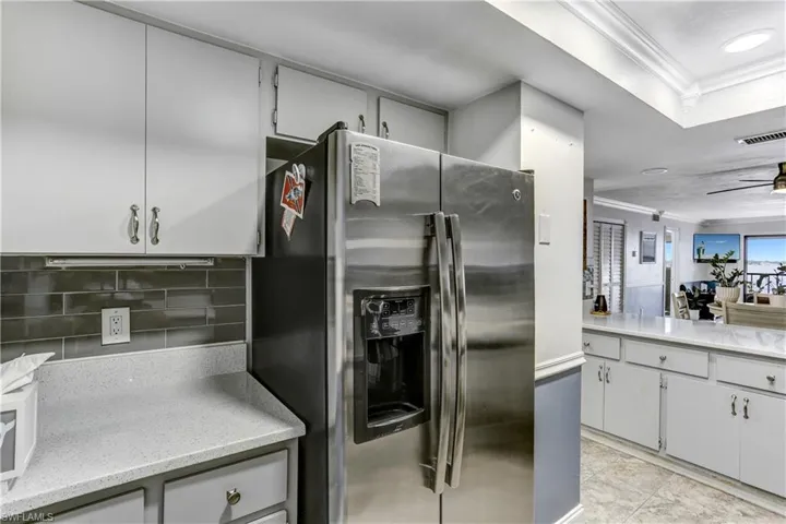 Kitchen featuring crown molding, stainless steel fridge with ice dispenser, light stone counters, ceiling fan, and open floor plan