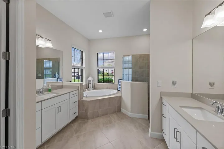 Full bath featuring walk in shower, a garden tub, two vanities, and a sink