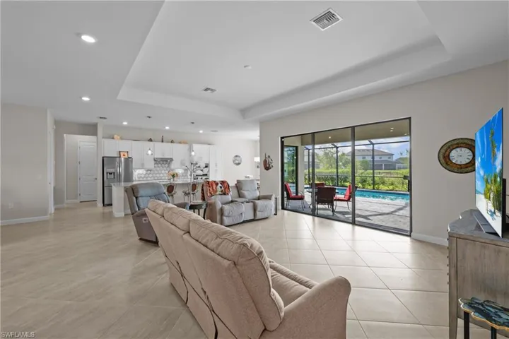 Living room with a tray ceiling, recessed lighting, light tile patterned floors, baseboards, and visible vents