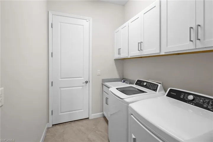 Clothes washing area with baseboards, a sink, washing machine and dryer, and cabinet space