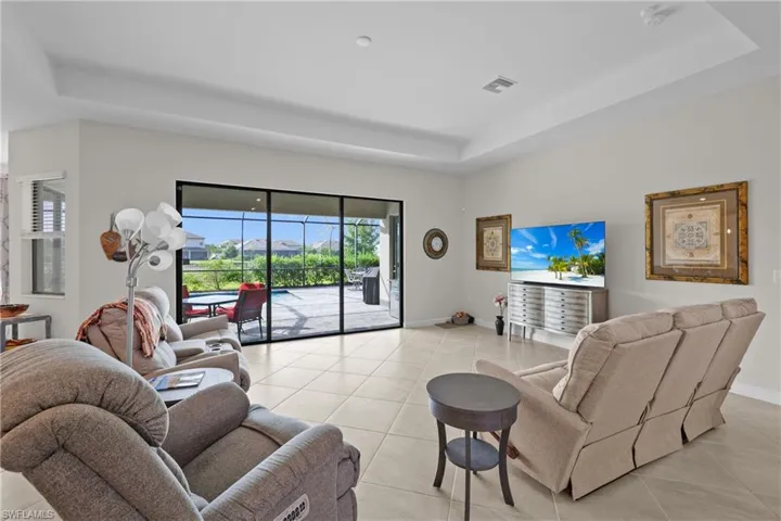 Living area with light tile patterned floors, baseboards, a tray ceiling, and visible vents