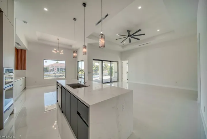 Kitchen with a tray ceiling, hanging light fixtures, a kitchen island with sink, white cabinets, and modern cabinets