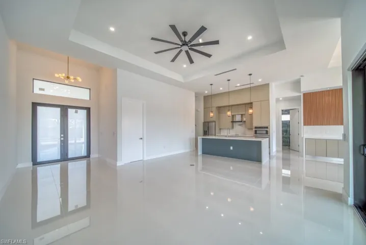 Unfurnished living room featuring french doors, a chandelier, a tray ceiling, plenty of natural light, and recessed lighting
