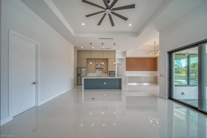 Unfurnished living room with a chandelier, a tray ceiling, a ceiling fan, light tile patterned floors, and recessed lighting
