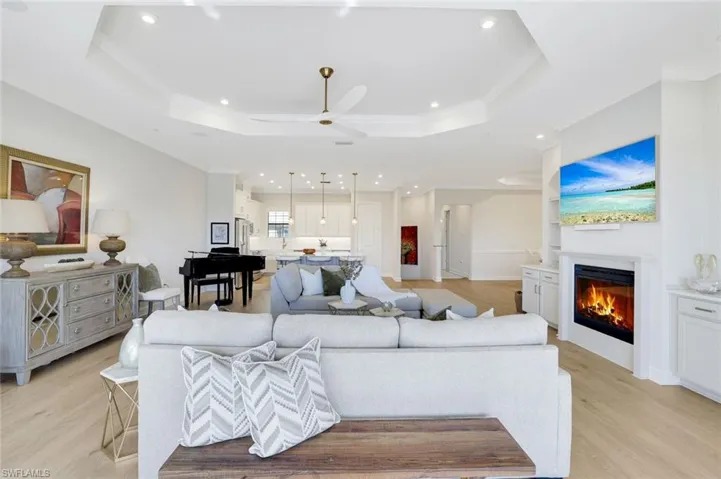 Open-concept living area featuring a tray ceiling, recessed lighting, wood-finish flooring, and a fireplace with built-in cabinetry