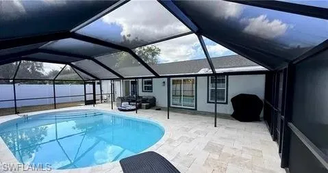 Screened enclosure featuring an in-ground pool, expansive paved patio, and white privacy fencing