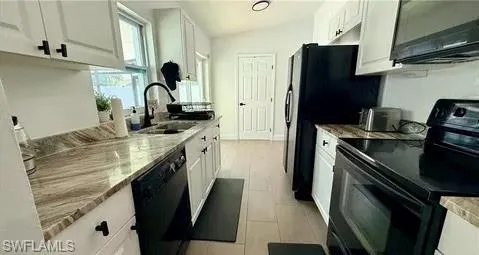 White cabinetry with black hardware, stone-finish countertops, tile flooring, black appliances, and a vaulted ceiling