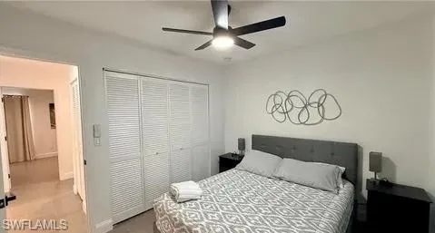 White walls with a ceiling fan, louvered closet doors, and wood-finish flooring