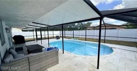 Screened-in pool area featuring an oval-shaped pool, a large patio with light-toned pavers, and a white privacy fence