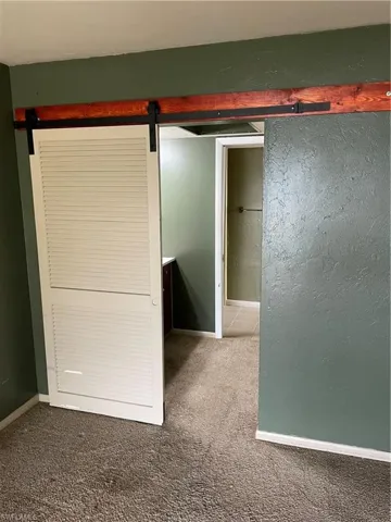 Unfurnished bedroom with a barn door and carpet floors
