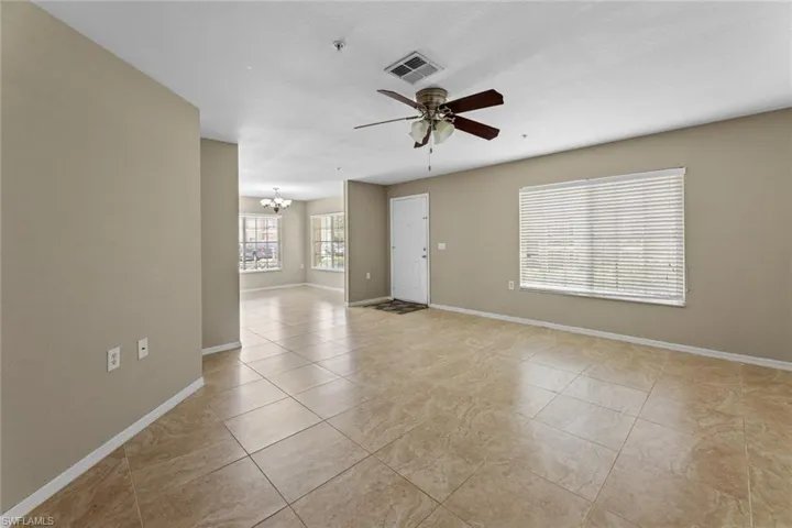 Empty room with a chandelier, ceiling fan, light tile patterned flooring, and a pendent fire sprinkler