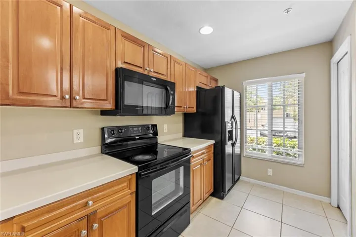 Kitchen featuring black appliances, light countertops, light tile patterned floors, brown cabinets, and recessed lighting