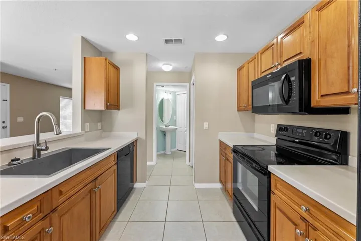 Kitchen featuring black appliances, light tile patterned floors, light countertops, brown cabinets, and recessed lighting