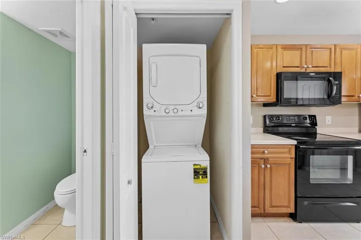 Washroom with stacked washer / dryer and light tile patterned floors