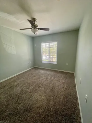 Carpeted spare room featuring a ceiling fan and baseboards