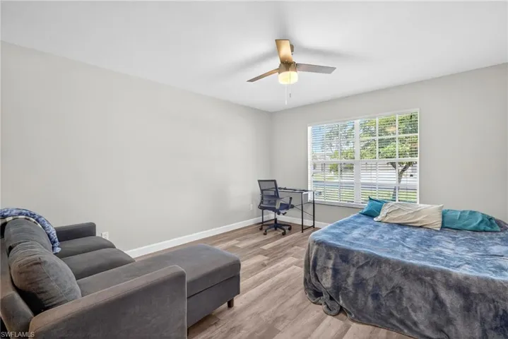 Room featuring wood-finish flooring, a multi-pane window, and a central ceiling fan with integrated lighting
