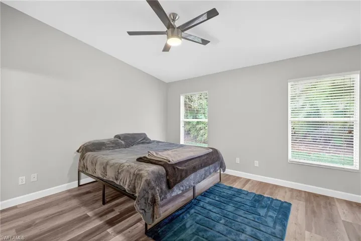 Vaulted ceiling featuring a central brushed-nickel finish ceiling fan, wood-finish flooring, and multiple dual-pane windows with horizontal blinds