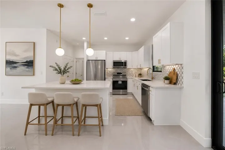 Contemporary kitchen featuring a large island with pendant lighting, white cabinetry, stainless steel appliances, and a decorative tile backsplash