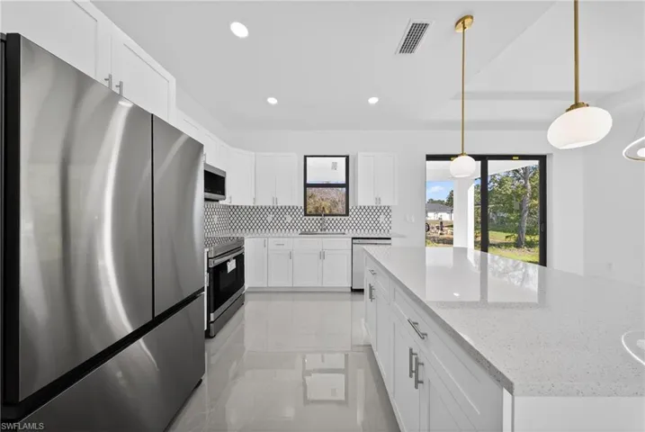 Kitchen featuring stainless steel appliances, white cabinets, a center island, light stone countertops, and pendant lighting