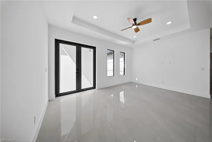 Empty room featuring ceiling fan, recessed lighting, french doors, light marble finish floors, and a raised ceiling