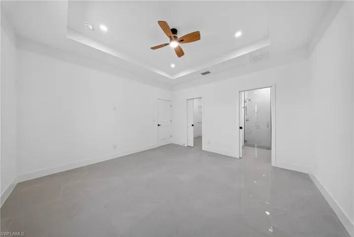 Unfurnished bedroom featuring ceiling fan, a tray ceiling, recessed lighting, light marble finish flooring, and a walk in closet