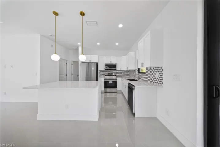 Kitchen with stainless steel appliances, white cabinets, tasteful backsplash, a center island, and light stone countertops