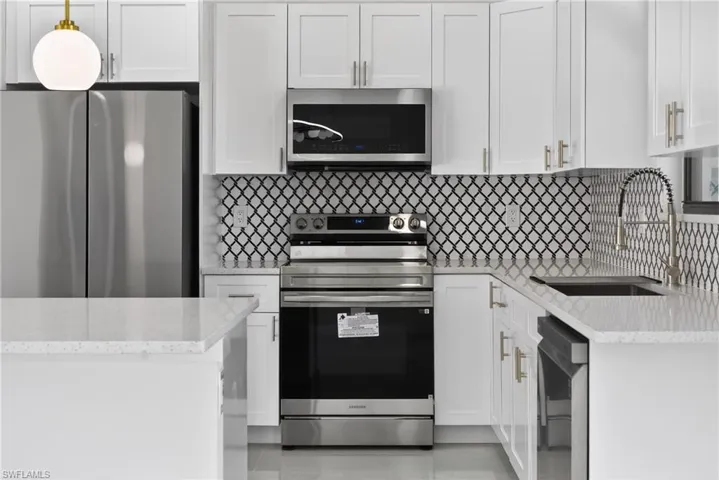 Kitchen with stainless steel appliances, white cabinets, light stone counters, and decorative backsplash