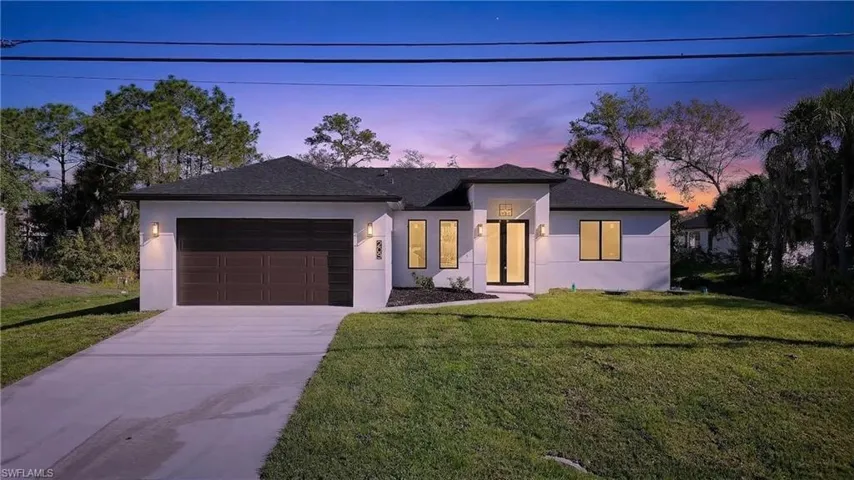 View of front of property with stucco siding, a front yard, a garage, and driveway