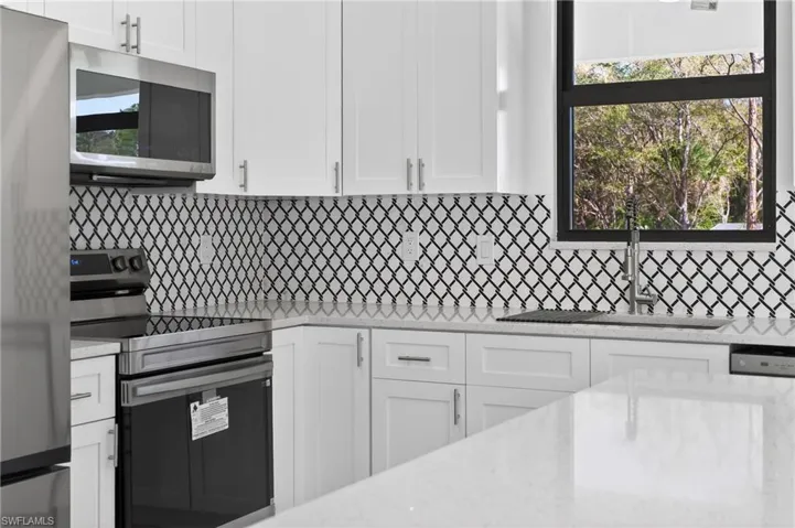 Kitchen with stainless steel appliances, white cabinetry, and light stone counters