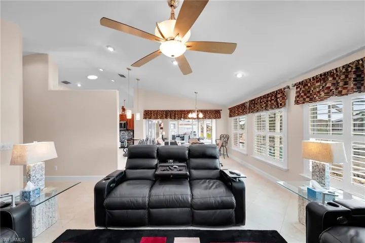 Living room featuring ceiling fan with notable chandelier, light tile patterned floors, and lofted ceiling