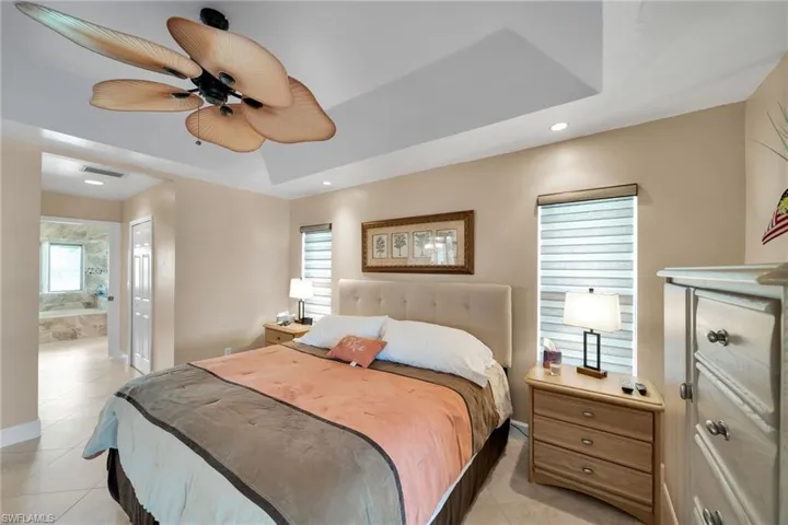 Bedroom featuring multiple windows, ensuite bathroom, light tile patterned floors, and ceiling fan