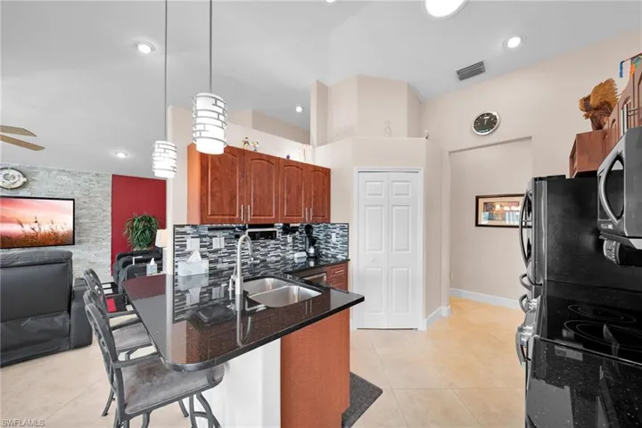 Kitchen with light tile patterned floors, backsplash, stainless steel appliances, decorative light fixtures, and a kitchen bar