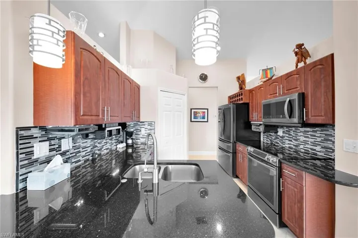 Kitchen with stainless steel appliances, hanging light fixtures, decorative backsplash, sink, and dark stone countertops