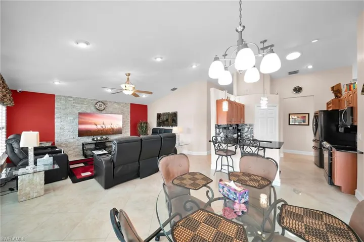 Dining area featuring ceiling fan with notable chandelier, lofted ceiling, and light tile patterned floors