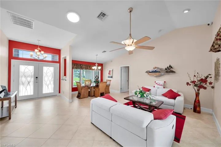 Living room featuring light tile patterned flooring, high vaulted ceiling, french doors, and ceiling fan with notable chandelier
