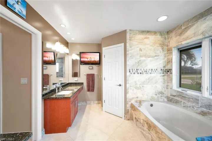 Bathroom featuring tile patterned flooring, tiled bath, and vanity