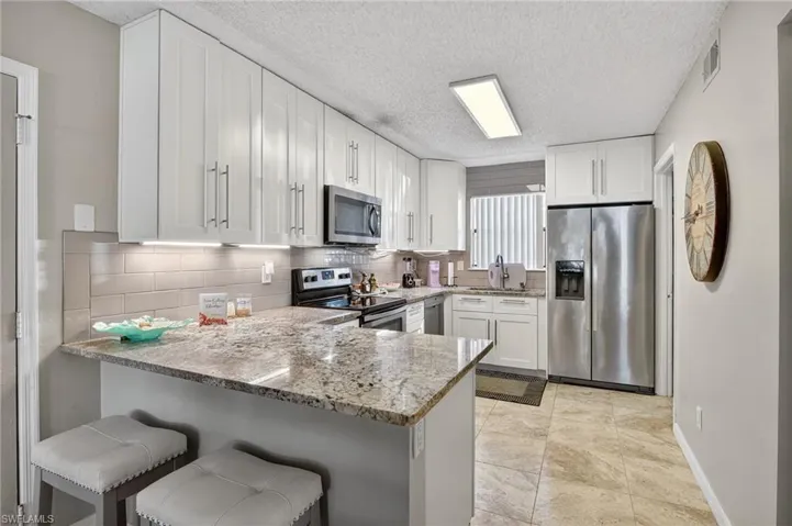 Kitchen featuring appliances with stainless steel finishes, light stone counters, white cabinets, a breakfast bar area, and a peninsula