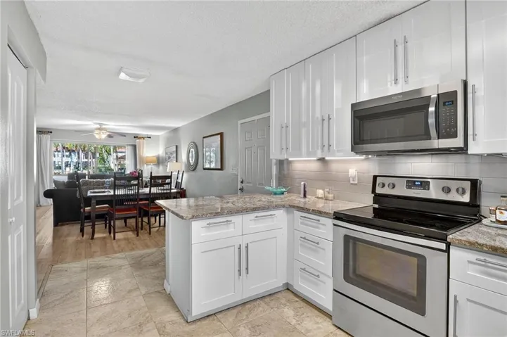 Kitchen with appliances with stainless steel finishes, white cabinets, a peninsula, backsplash, and light stone countertops