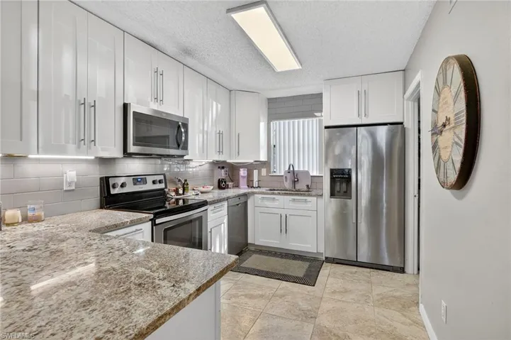 Kitchen featuring appliances with stainless steel finishes, white cabinets, backsplash, light stone countertops, and a textured ceiling