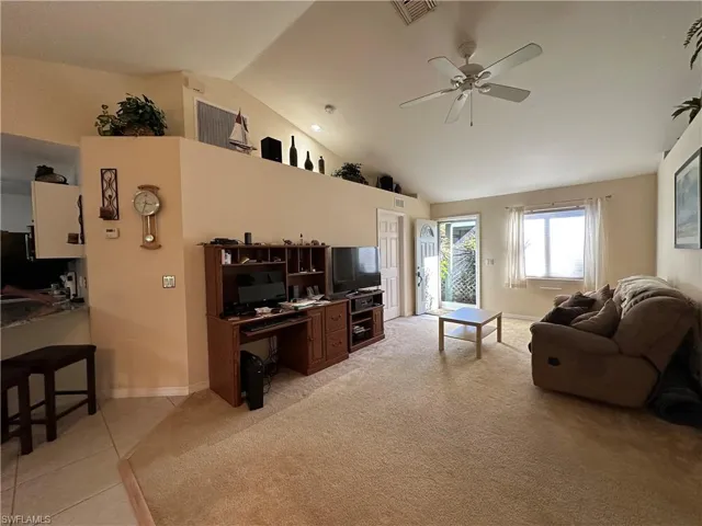 Living room with lofted ceiling, light tile patterned floors, and ceiling fan