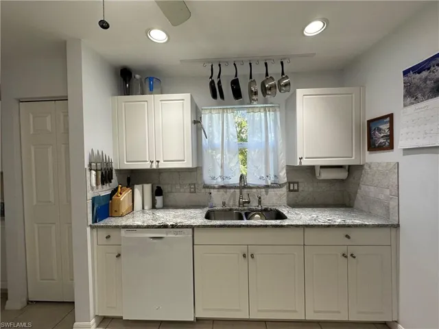 Kitchen with dishwasher, sink, light stone countertops, and light tile patterned floors