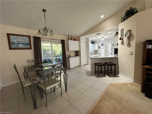 Tiled dining space with ceiling fan with notable chandelier and vaulted ceiling