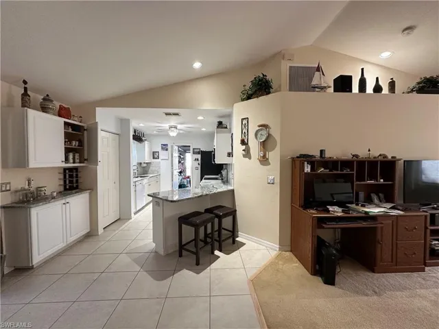 Kitchen with vaulted ceiling, a breakfast bar area, white cabinets, kitchen peninsula, and light granite countertops