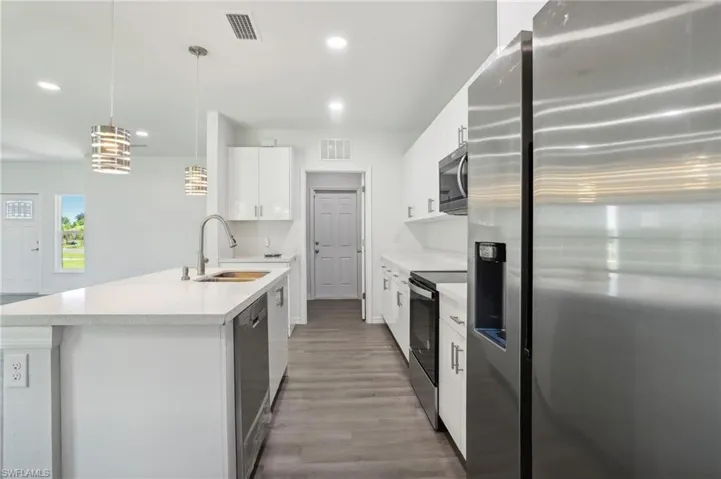 Kitchen featuring hardwood / wood-style floors, sink, appliances with stainless steel finishes, white cabinetry, and hanging light fixtures