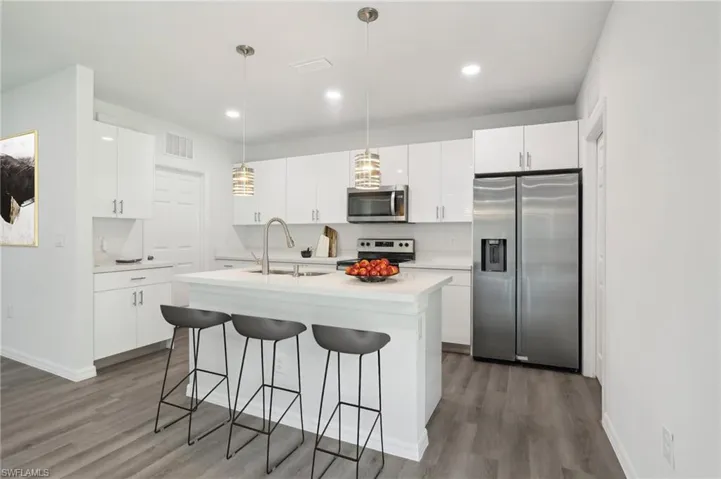 Kitchen with appliances with stainless steel finishes, sink, a kitchen island with sink, white cabinets, and wood-type flooring