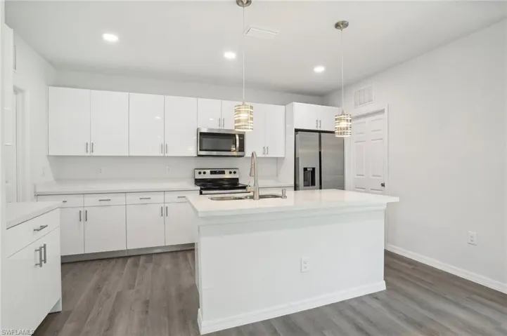 Kitchen featuring appliances with stainless steel finishes, light hardwood / wood-style flooring, decorative light fixtures, white cabinetry, and a center island with sink