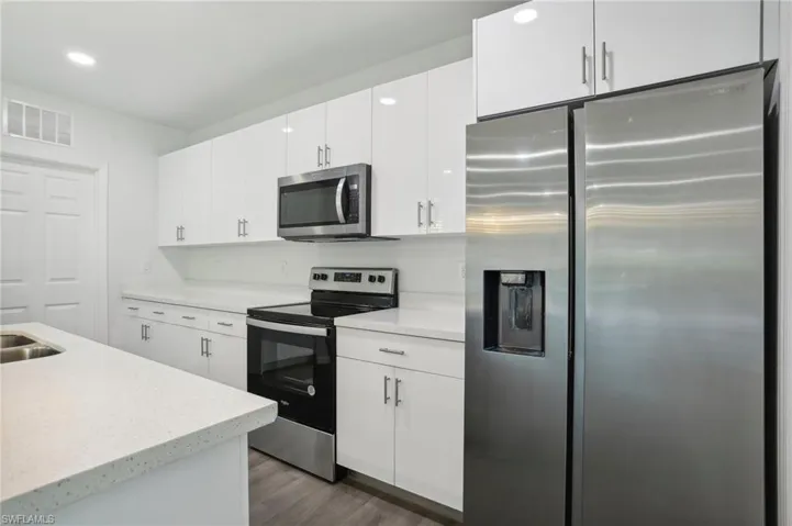 Kitchen with appliances with stainless steel finishes, light stone countertops, hardwood / wood-style floors, and white cabinetry