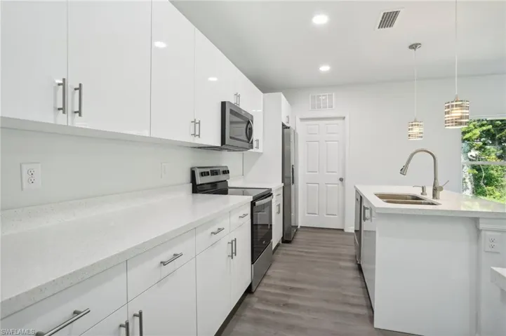 Kitchen featuring sink, hanging light fixtures, wood-type flooring, white cabinetry, and stainless steel appliances